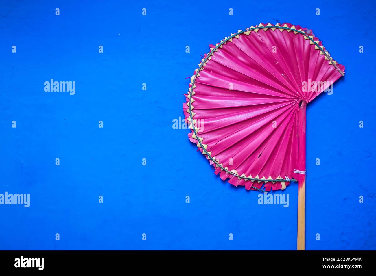 Ventilatori a mano Palm Leaf isolati con sfondo blu. Ventilatori a mano a foglia di palma rosa fatti a mano disponibili in vendita nella stagione estiva. Foto Stock