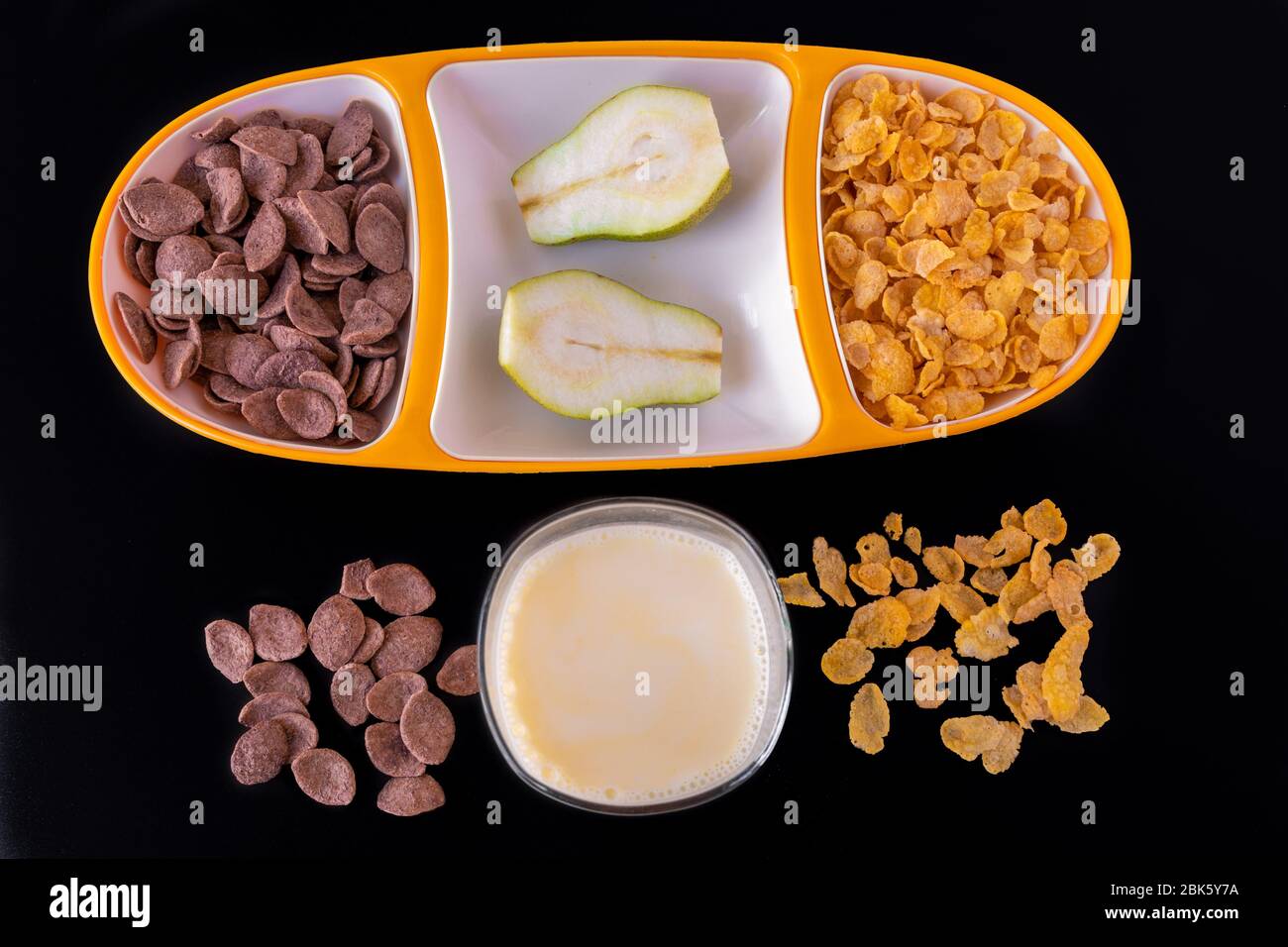 Cereali in vassoio giallo con fette di latte e pera isolate su sfondo grigio nero, una deliziosa e sana colazione dietetica. V superiore Foto Stock