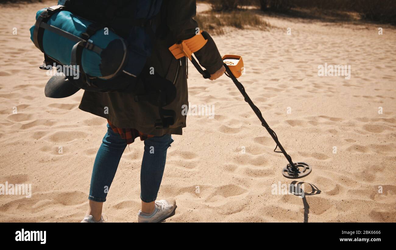 Donna irriconoscibile con metal detector alla ricerca di manufatti a piedi sulla spiaggia di sabbia in giornata di sole. Foto Stock