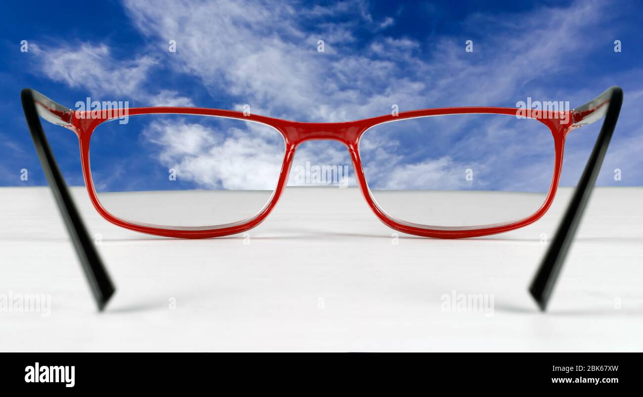 Cielo blu visto attraverso un paio di occhiali che giacciono su un tavolo bianco Foto Stock