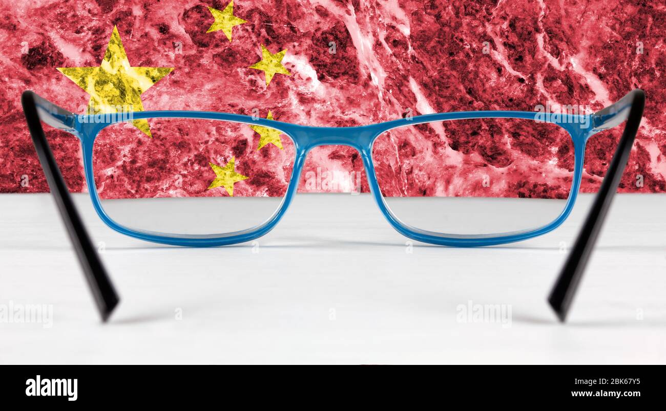 Bandiera creativa della Cina vista attraverso un paio di occhiali che giace su un tavolo bianco Foto Stock