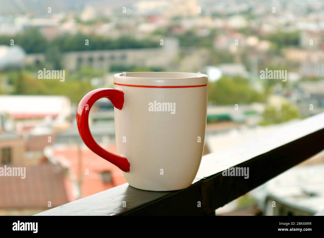 Chiosare una tazza di caffè sul balcone contro la vista della città sfocata Foto Stock