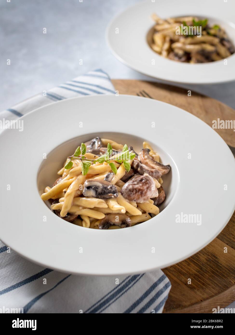 Pasta di funghi all'aglio servita in una ciotola bianca su un asse di legno. DOF poco profondo Foto Stock