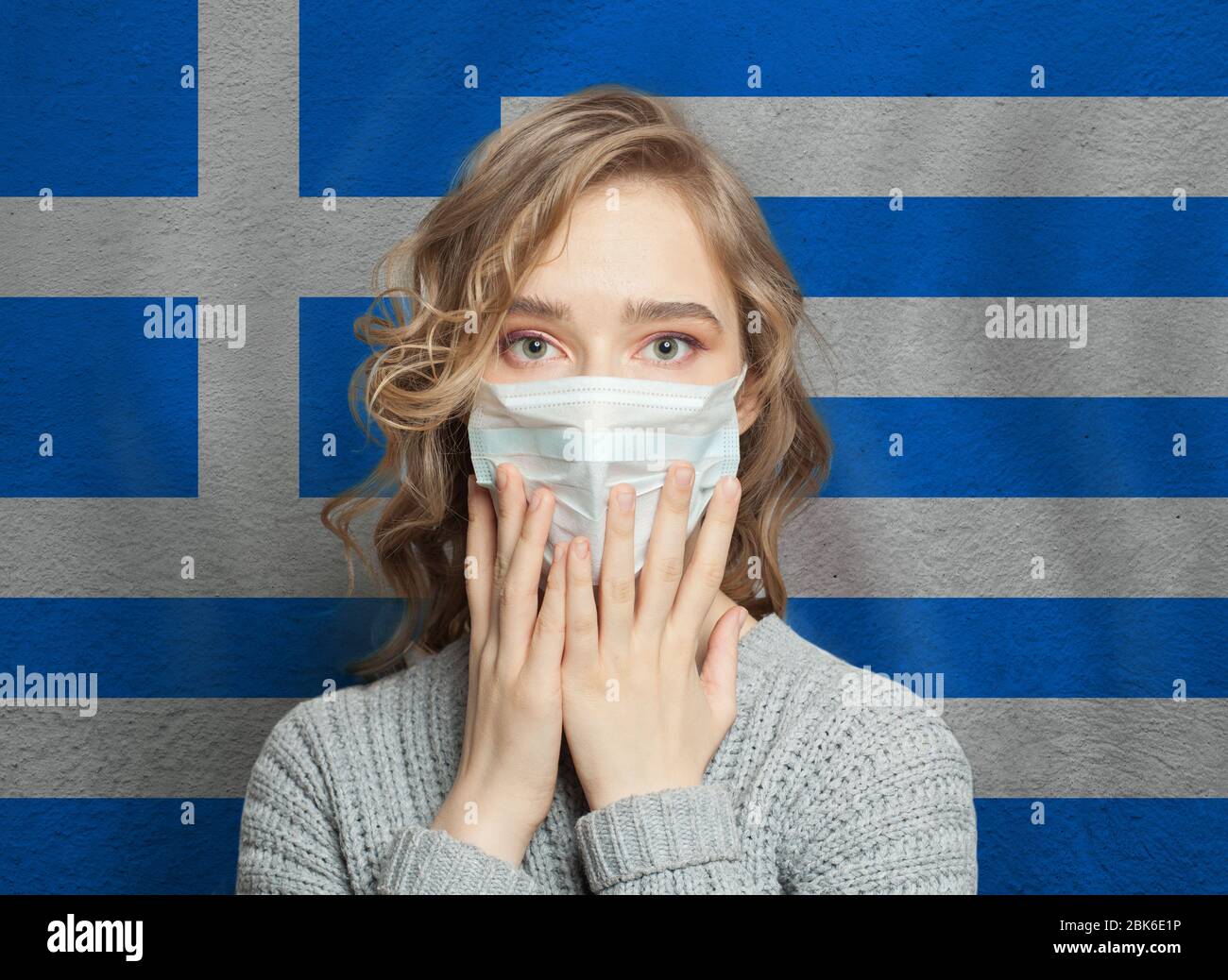 Donna impaurita in maschera medica sullo sfondo della bandiera greca. Influenza epidemica e violenza domestica in Grecia concetto Foto Stock