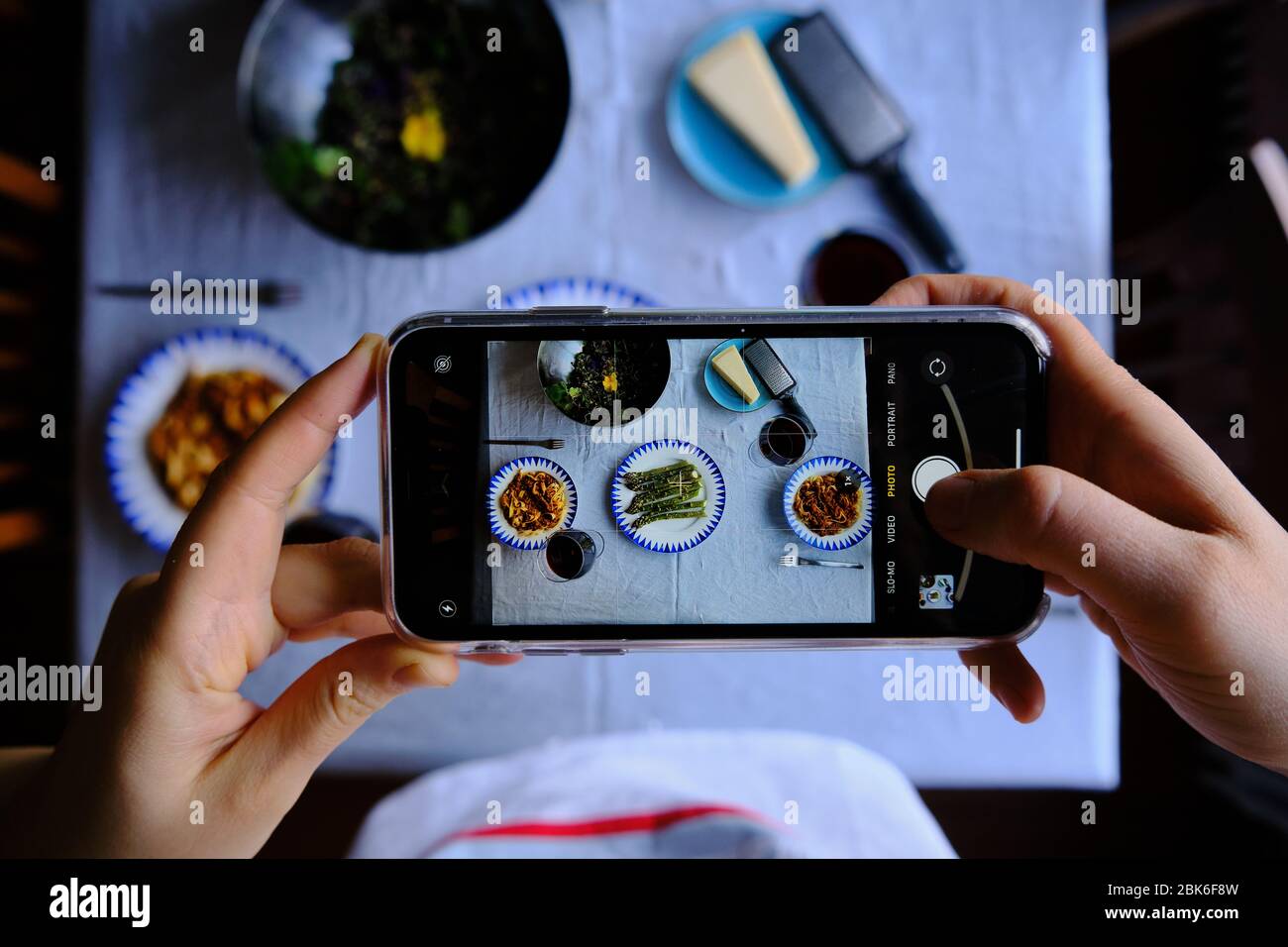 Scattare foto al tavolo del pranzo con tagliatelle bolognese, asparagi e insalata con uno smartphone. Concetto per la fotografia alimentare con smartphone. Foto Stock