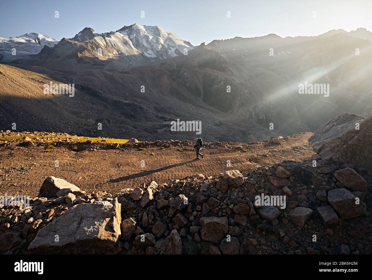 Escursionista con zaino è di camminare sulla strada con spettacolari montagne a sfondo Foto Stock