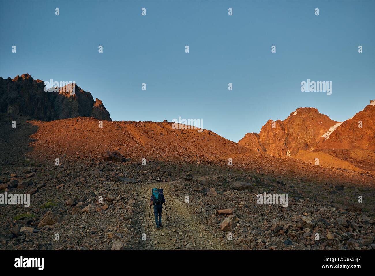 Escursionista con grande zaino è di camminare sulla strada con spettacolari montagne al tramonto Foto Stock