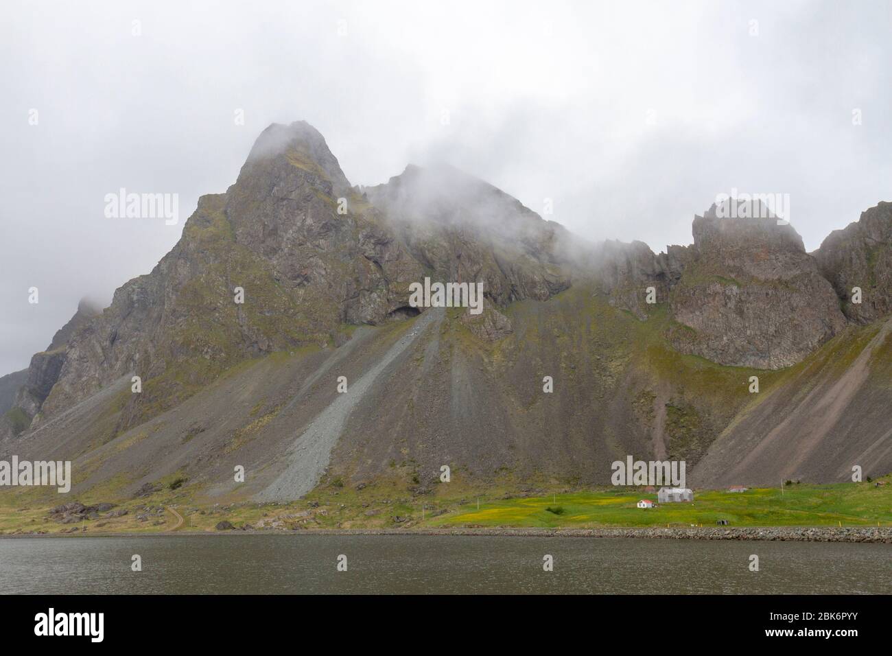 Classica vista islandese di un piccolo edificio contro una massiccia scarpata sulla Route 1 nel sud dell'islanda, Foto Stock