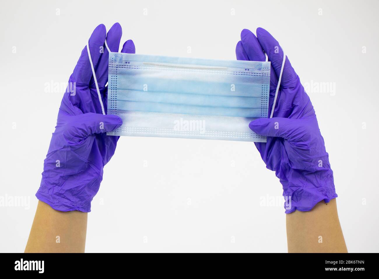 Chiudere la maschera medica monouso nelle mani del medico con guanti di gomma blu Foto Stock