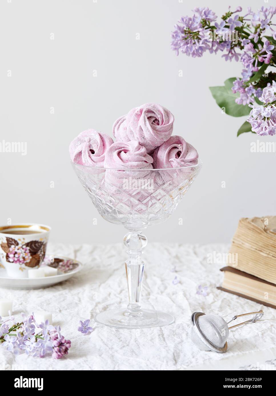 Viola dolce fatto in casa Zephyr o Marshmallow da ribes nero vicino ai fiori di lilla, vecchi libri e tazza di caffè su bianco da tavola e backgrou bianco Foto Stock