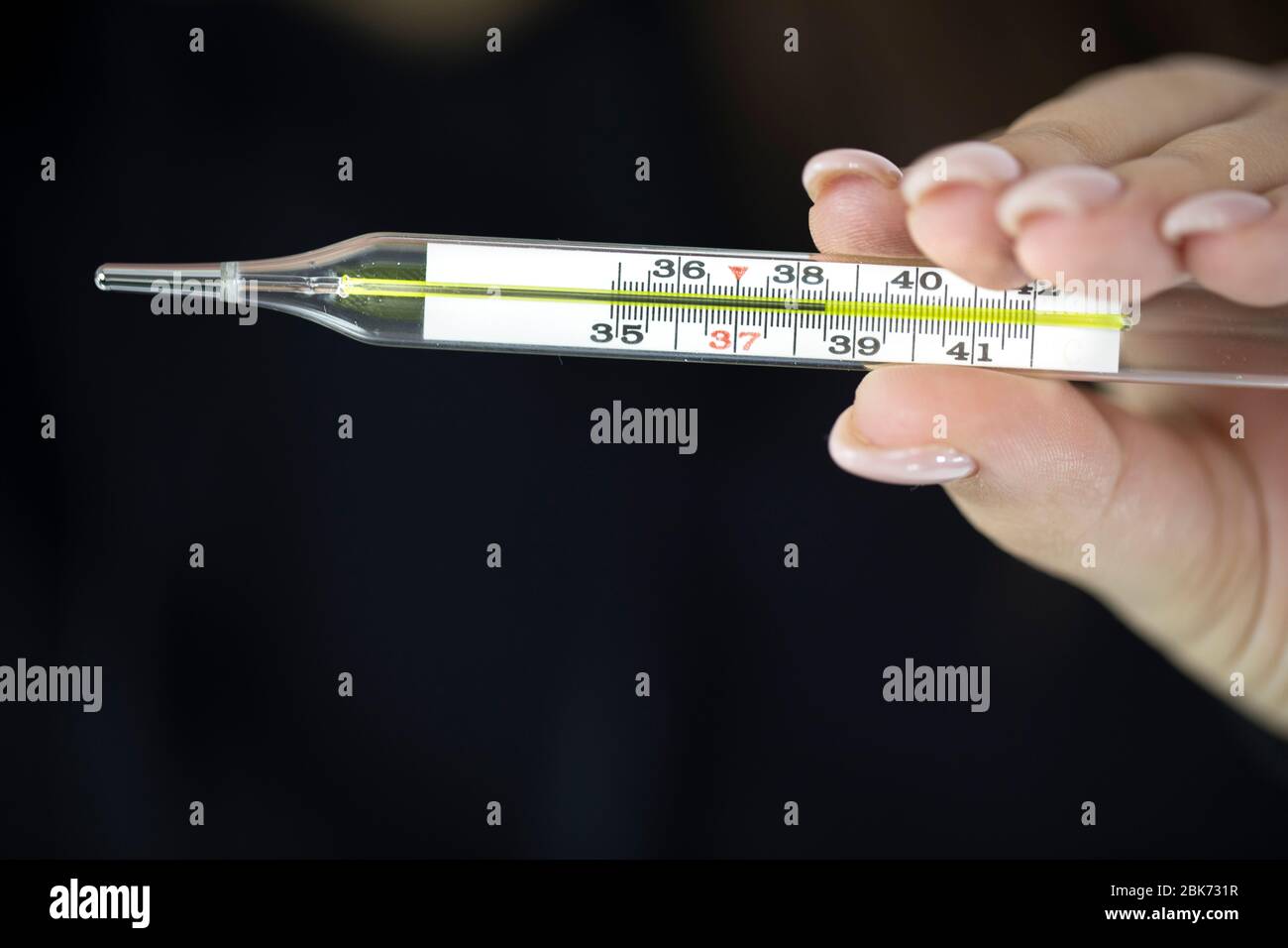 La femmina tiene in mano un termometro a mercurio che mostra 38,5 gradi,  febbre alta Foto stock - Alamy