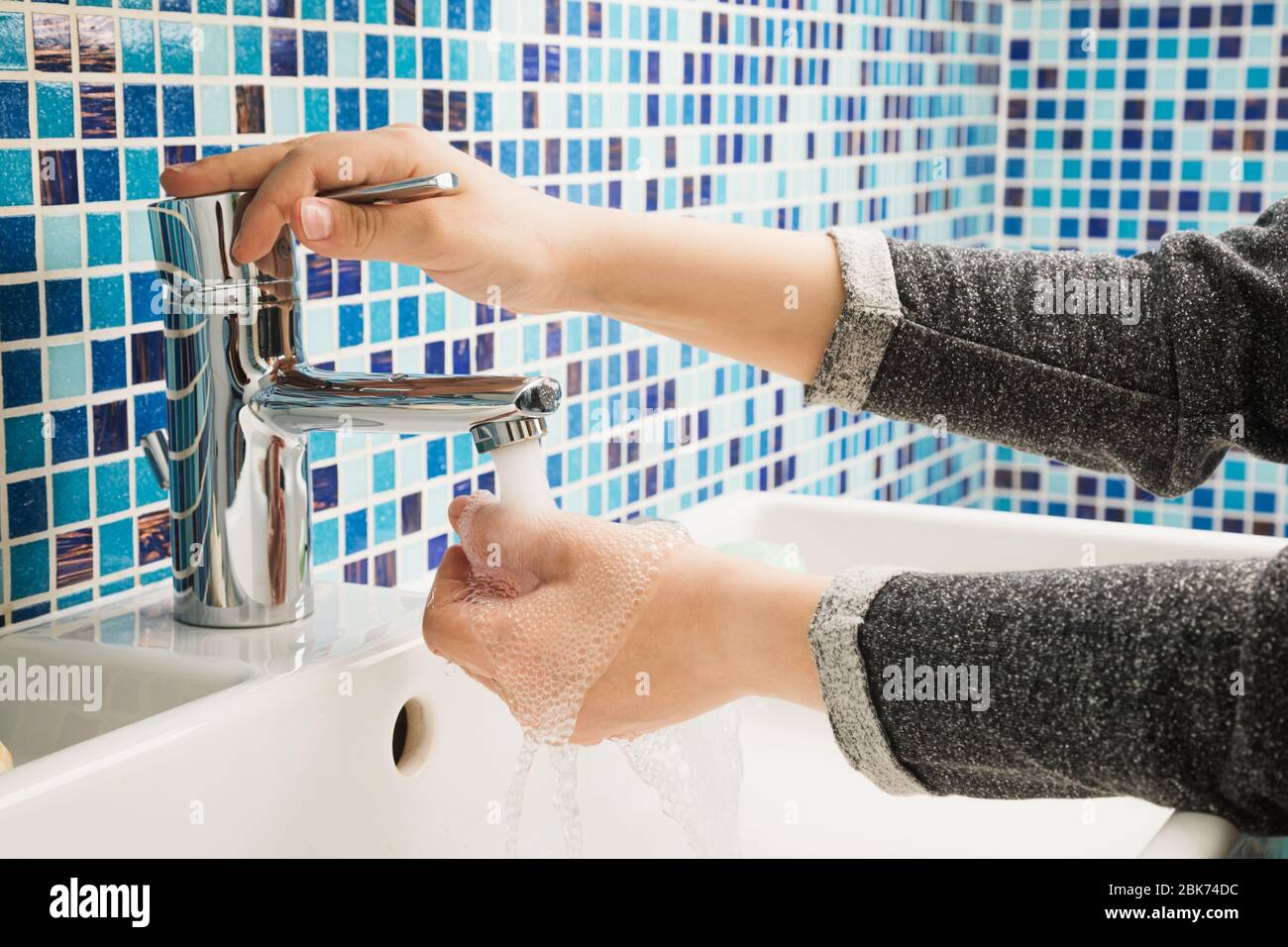 Il bambino apre il rubinetto dell'acqua per lavare le mani, effettuando le misure protettive di base contro la diffusione del virus COVID-19 Foto Stock