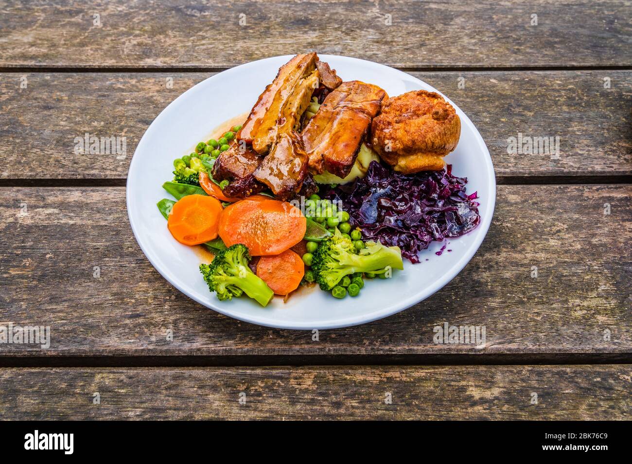 Piatto di Domenica arrosto su superficie di legno d'annata, tradizionale pasto britannico di carne arrosto, patate arrosto, budino Yorkshire, sugo di carne, salsa alla menta, verde Foto Stock