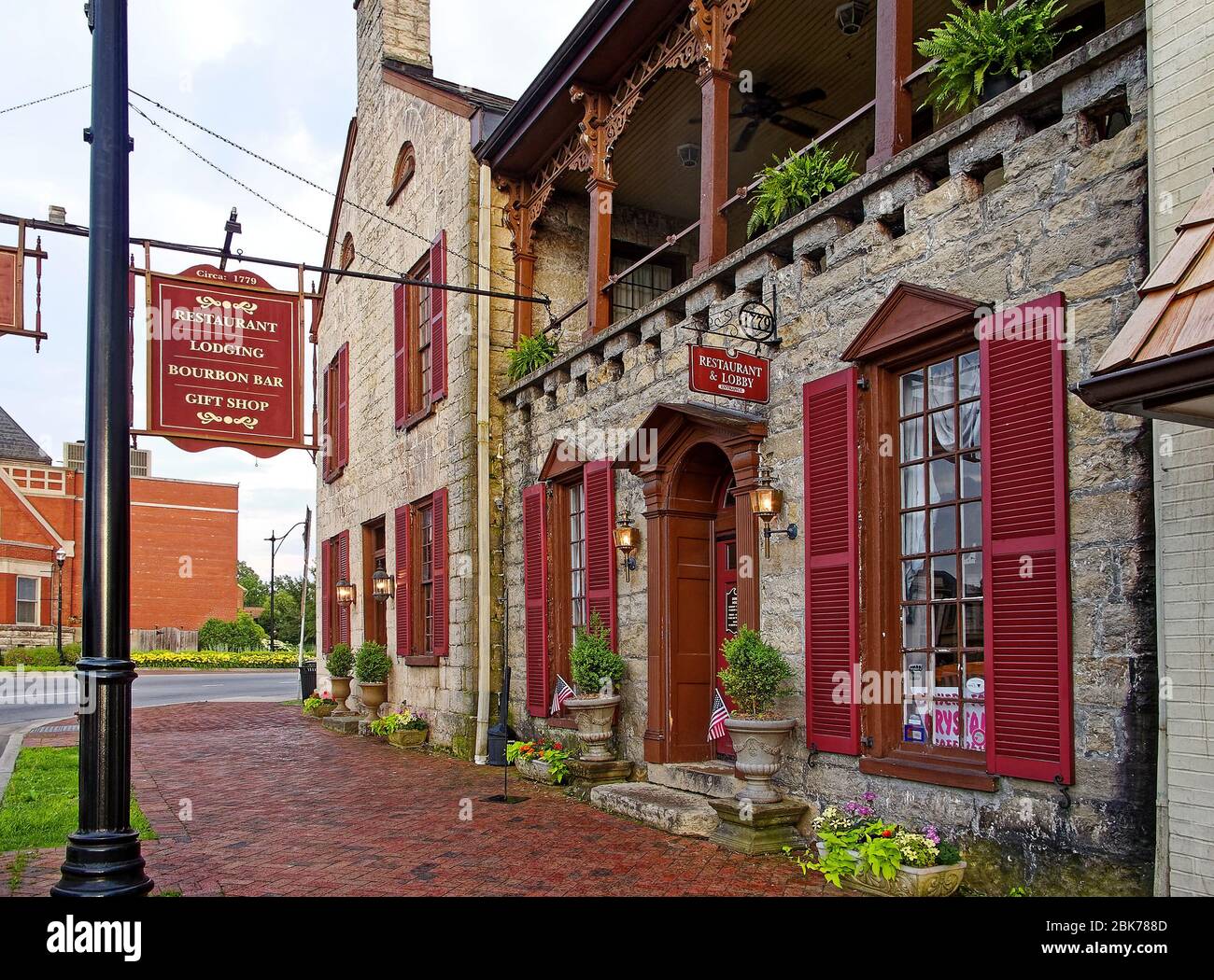 Edificio in pietra 1779; Talbot Tavern; balcone; marciapiede in mattoni; persiane rosse scure; crepuscolo; lanterne illuminate; vecchio; segni appesi, piante in vaso, Kentucky; U. Foto Stock