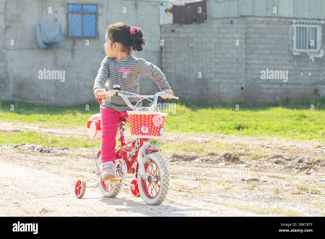 Bambina in bicicletta rossa a quattro ruote in strada sterrata guardando dietro, scappando in bicicletta Foto Stock