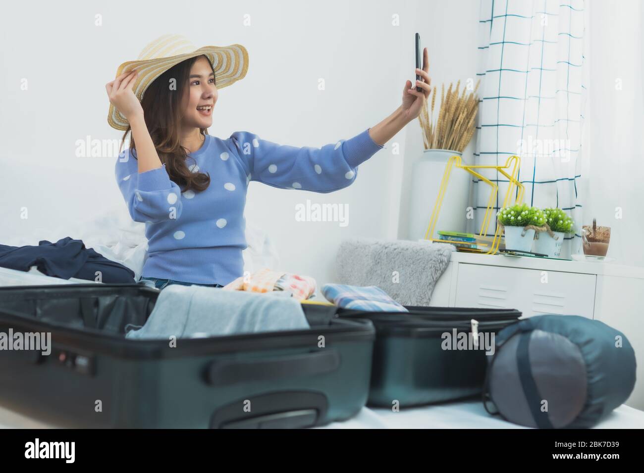 Preparazione e pianificazione del viaggio sul concetto di vacanza, tailandese e Asia donna felice guardando se stesso al telefono e imballaggio vestiti in valigia borsa t Foto Stock
