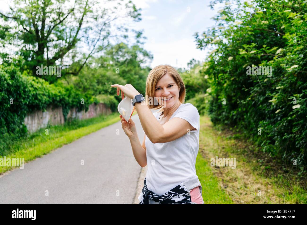 Una donna toglie la maschera in un parco sulla strada verde Foto Stock