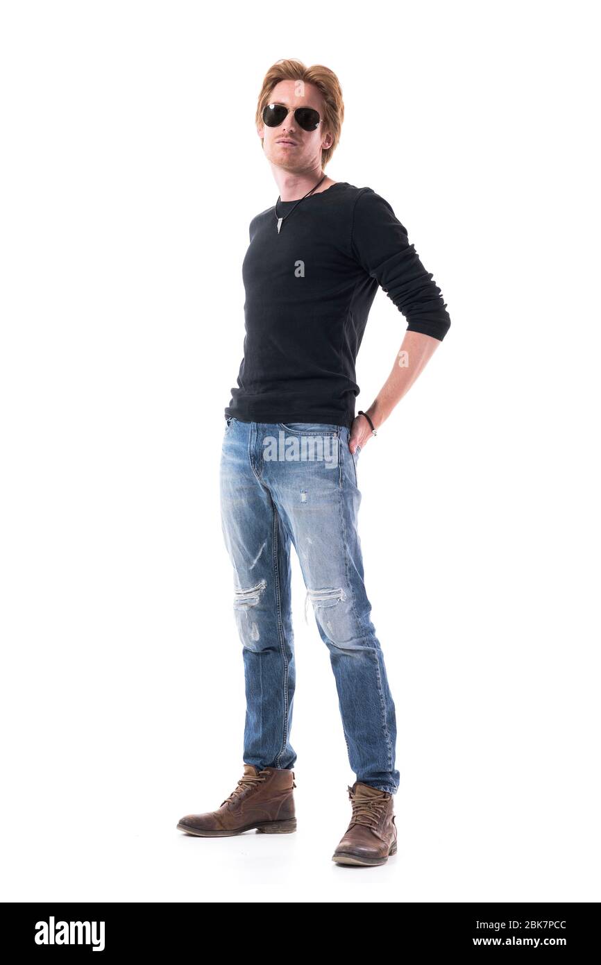 Attraente giovane capelli rossi uomo modello moda in jeans strappati e camicia nera indossando occhiali da sole. Corpo intero isolato su sfondo bianco. Foto Stock