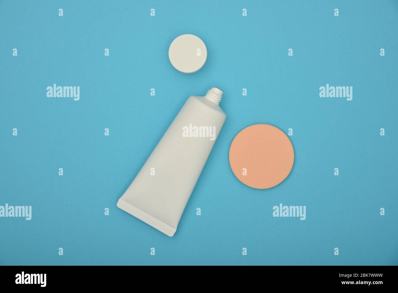 Primo piano un tubo bianco di crema di fondazione trucco e spugna beige su sfondo blu, vista superiore elevata, direttamente sopra Foto Stock