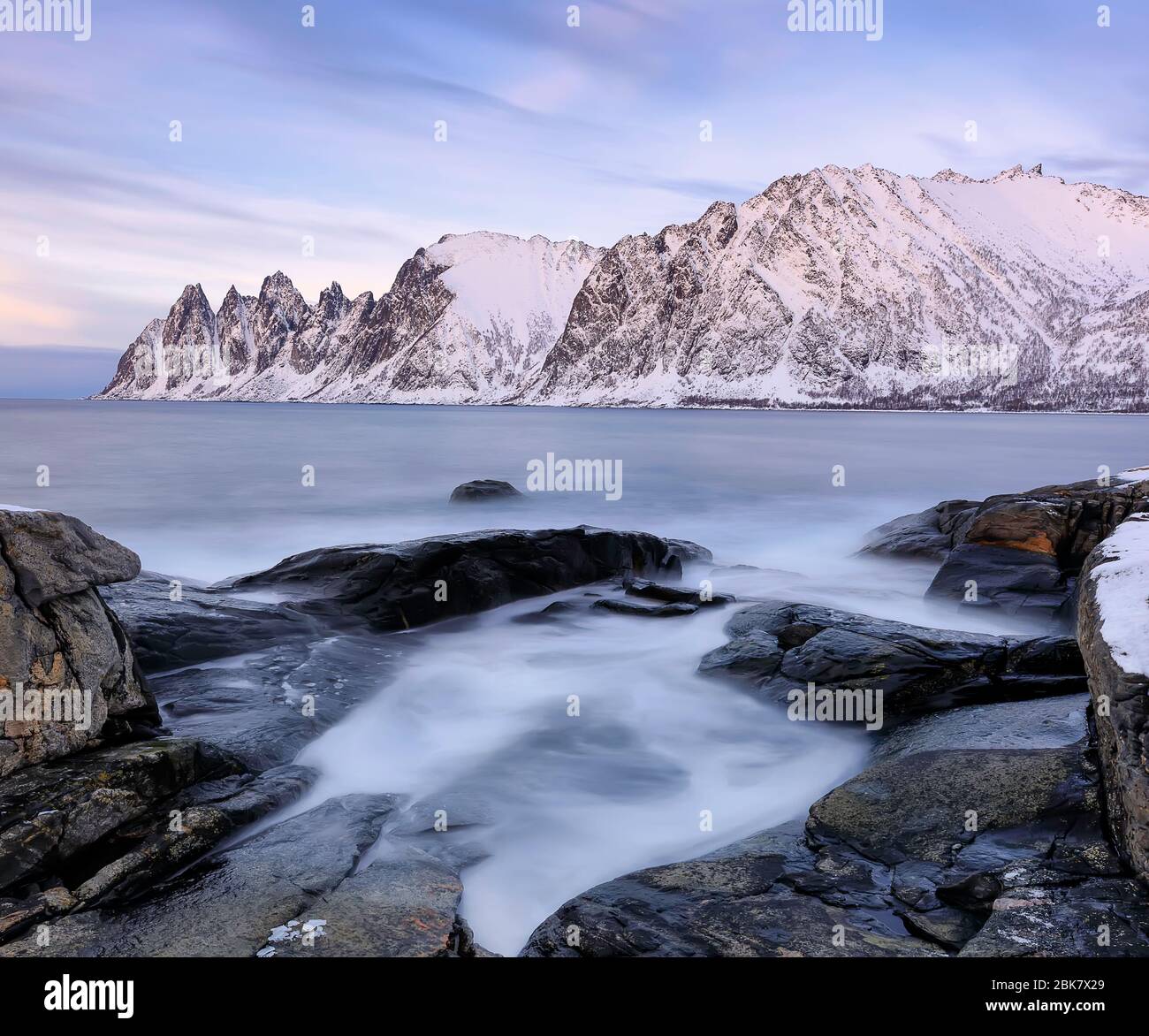 La spiaggia rocciosa e le onde ghiacciate in piscina sul Ersfjord. Isola di Senja nella regione di Troms nella Norvegia settentrionale. Scatto a lunga esposizione Foto Stock