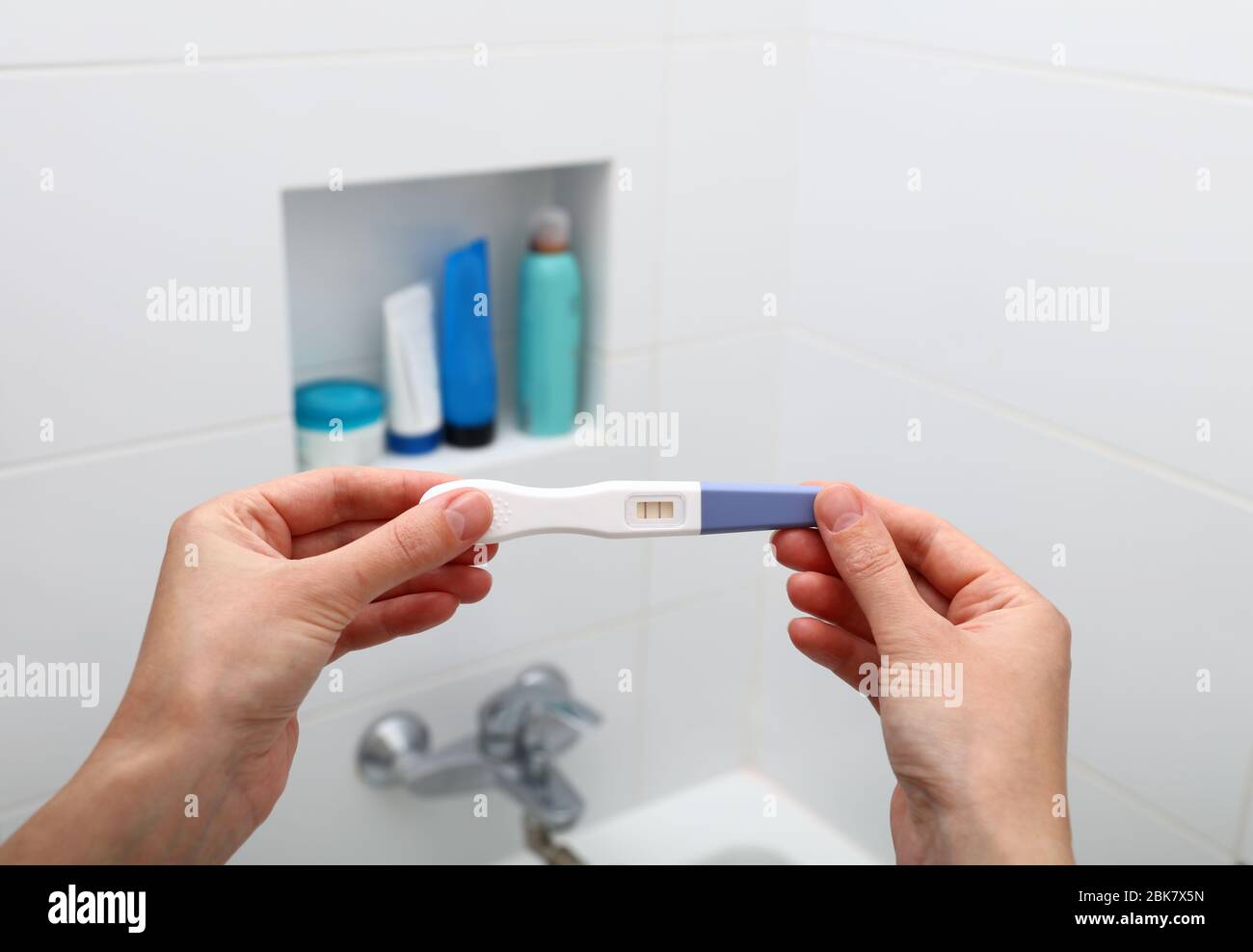 Primo piano donna mani tenendo test di gravidanza positivo in bagno, prospettiva personale, vista ad alto angolo Foto Stock