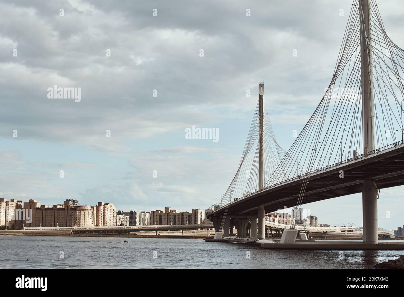 il cavo moderno ha sospeso il ponte sul fiume contro il cielo nuvoloso. Primo piano per la costruzione di ingegneria Foto Stock