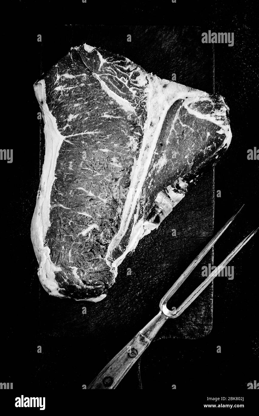 Bistecca premium cruda a T-bone invecchiata a secco su un tavolo da triturazione rustico. Carne di manzo di prima qualità USDA in bianco e nero. Foto Stock
