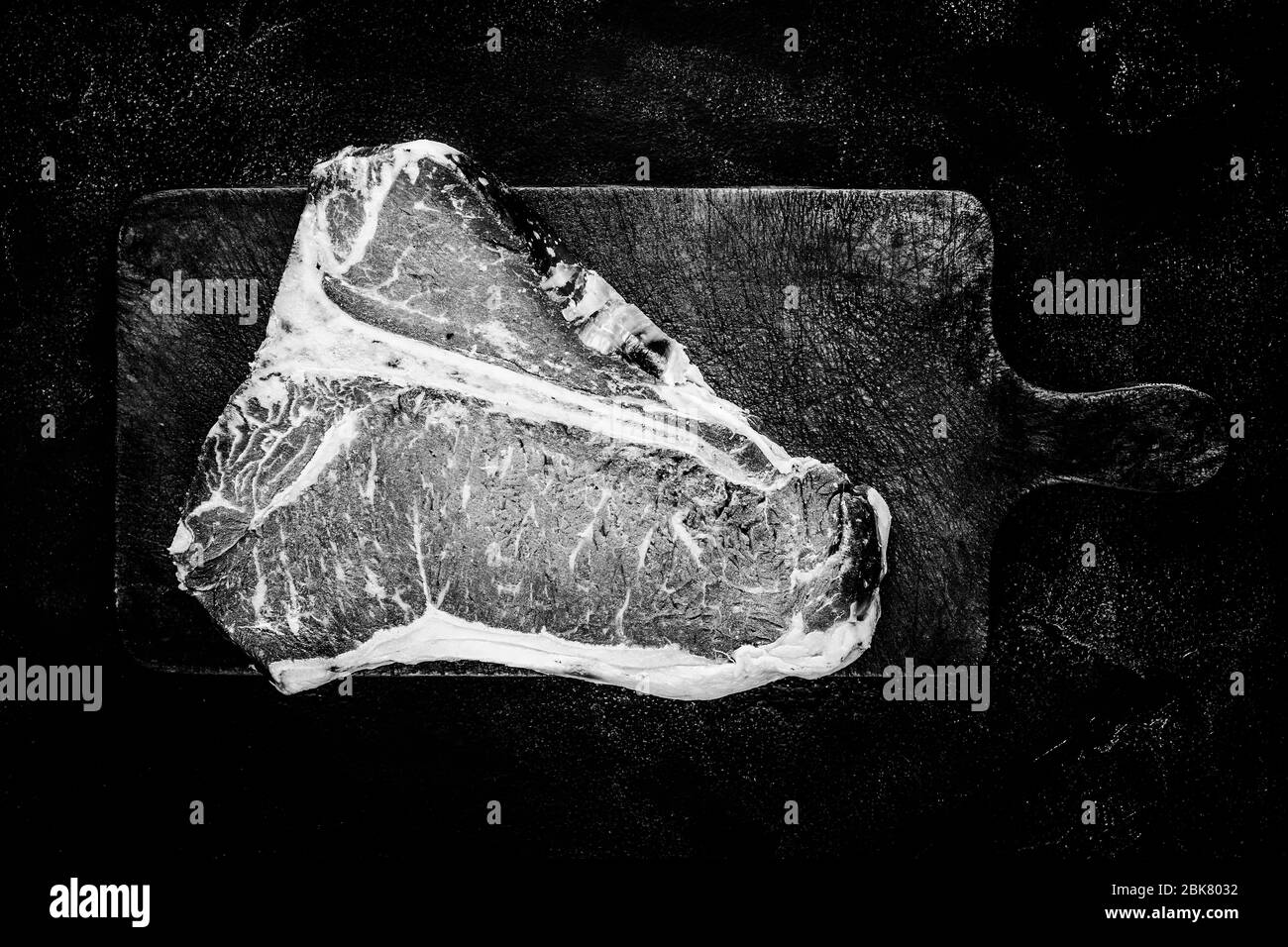 Bistecca premium cruda a T-bone invecchiata a secco su un tavolo da triturazione rustico. Carne di manzo di prima qualità USDA in bianco e nero. Foto Stock