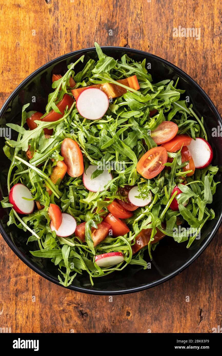 Insalata di rucola fresca con ravanelli, pomodori e peperoni rossi sul piatto. Vista dall'alto. Foto Stock
