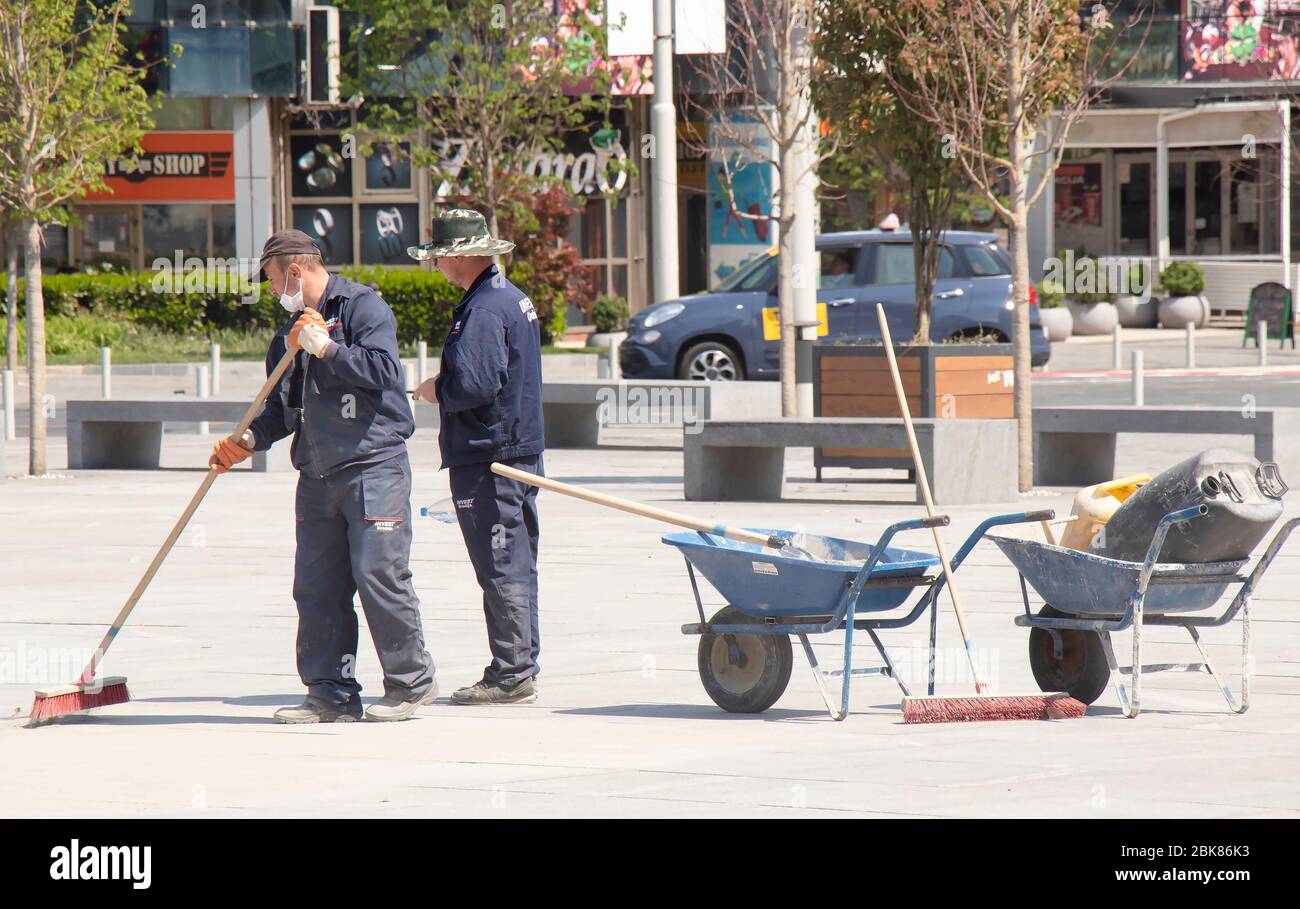 Belgrado, Serbia - 24 aprile 2020: Lavoratori edili riempendo i giunti in granito con sabbia utilizzando ginestra lunga, pavimentazione stradale finitura, carriola Foto Stock