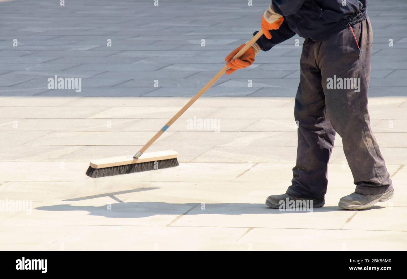 Lavoratore della pavimentazione che riempie i giunti del blocco con sabbia utilizzando una spazzatrice lunga, rifinendo la pavimentazione stradale in movimento sfocata Foto Stock