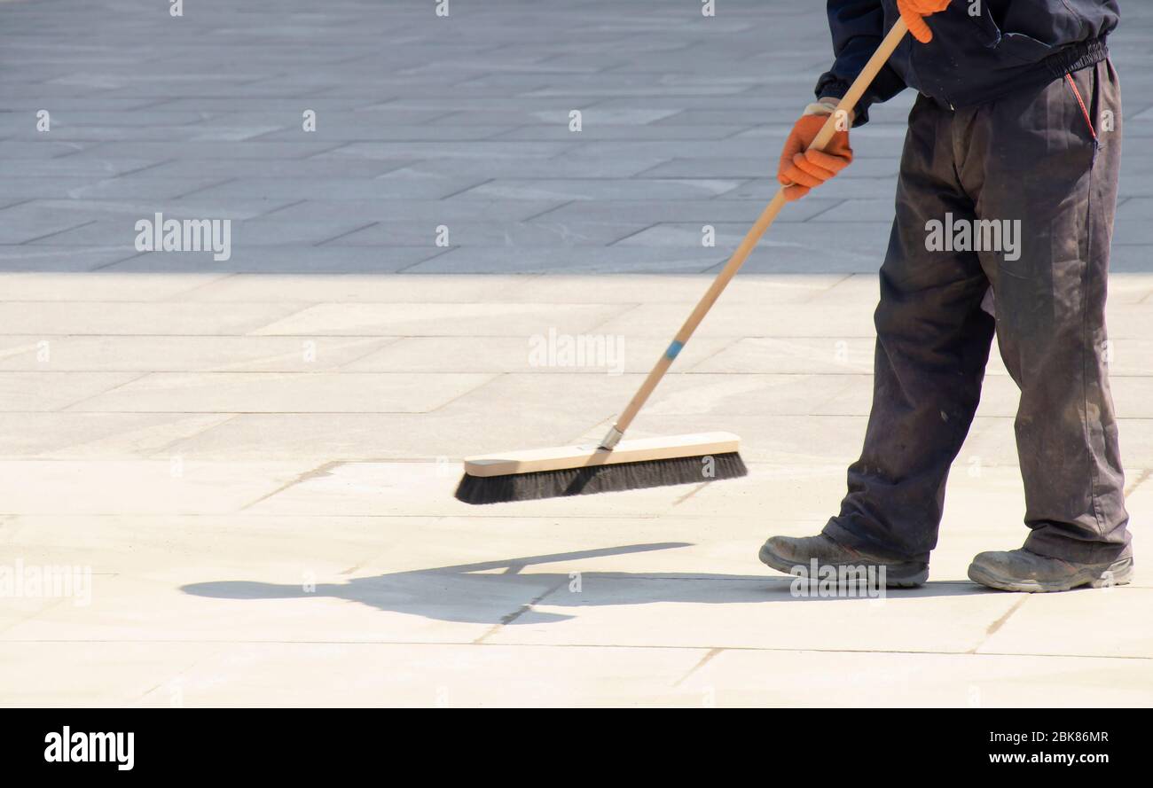 Lavoratore della pavimentazione che riempie i giunti del blocco con sabbia utilizzando una spazzatrice lunga, rifinendo la pavimentazione stradale in movimento sfocata Foto Stock
