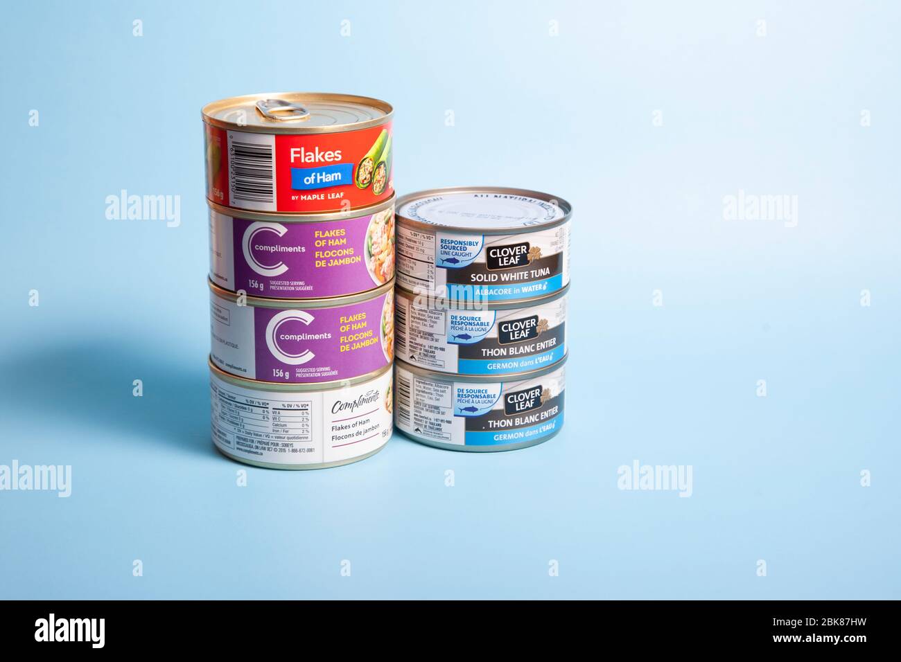 11 aprile 2020: Halifax, Canada - fiocchi di prosciutto e lattine di tonno bianco solido provenienti da diverse aziende su sfondo blu Foto Stock