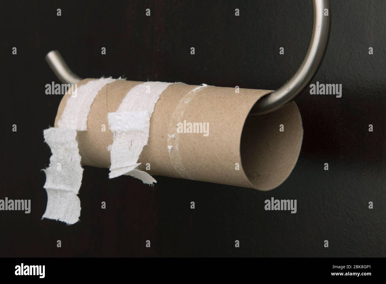 Un rotolo di carta igienica vuoto su un supporto contro una parete nera. Foto Stock