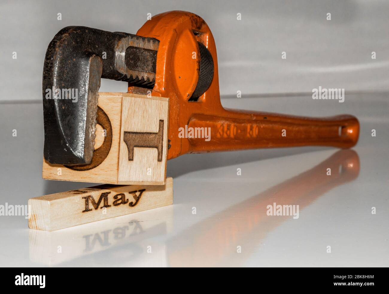 una chiave per tubi che comprime il cubo di legno 'primo di maggio' - tema del giorno del lavoro con cubi / blocchi di calendario in legno Foto Stock