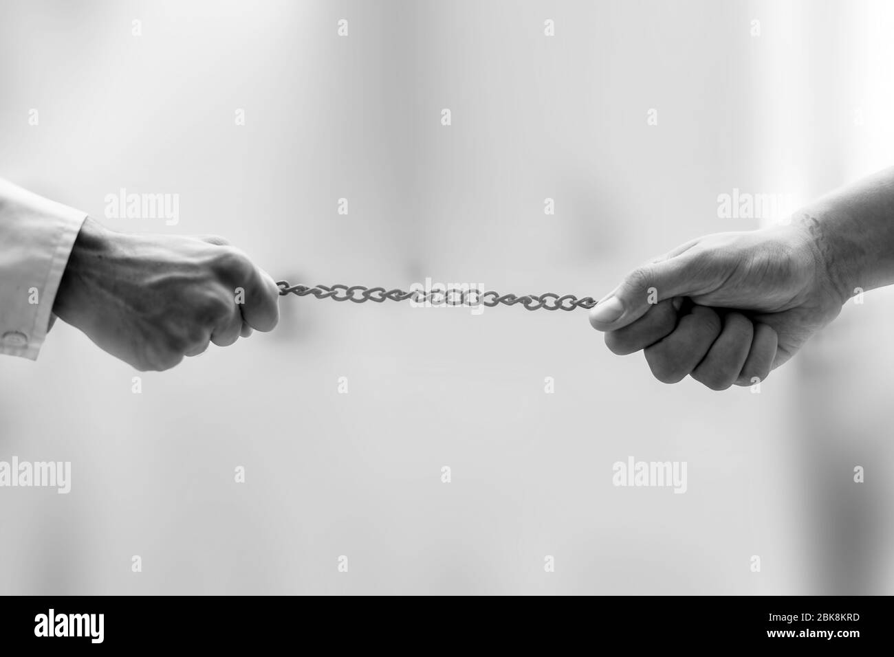 Colpo di due mani sull'estremità di una catena di metallo arrugginita che tira da entrambi i lati con sfondo sfocato e messa a fuoco selettiva. Mano maschile che gioca il rimorchiatore del Foto Stock