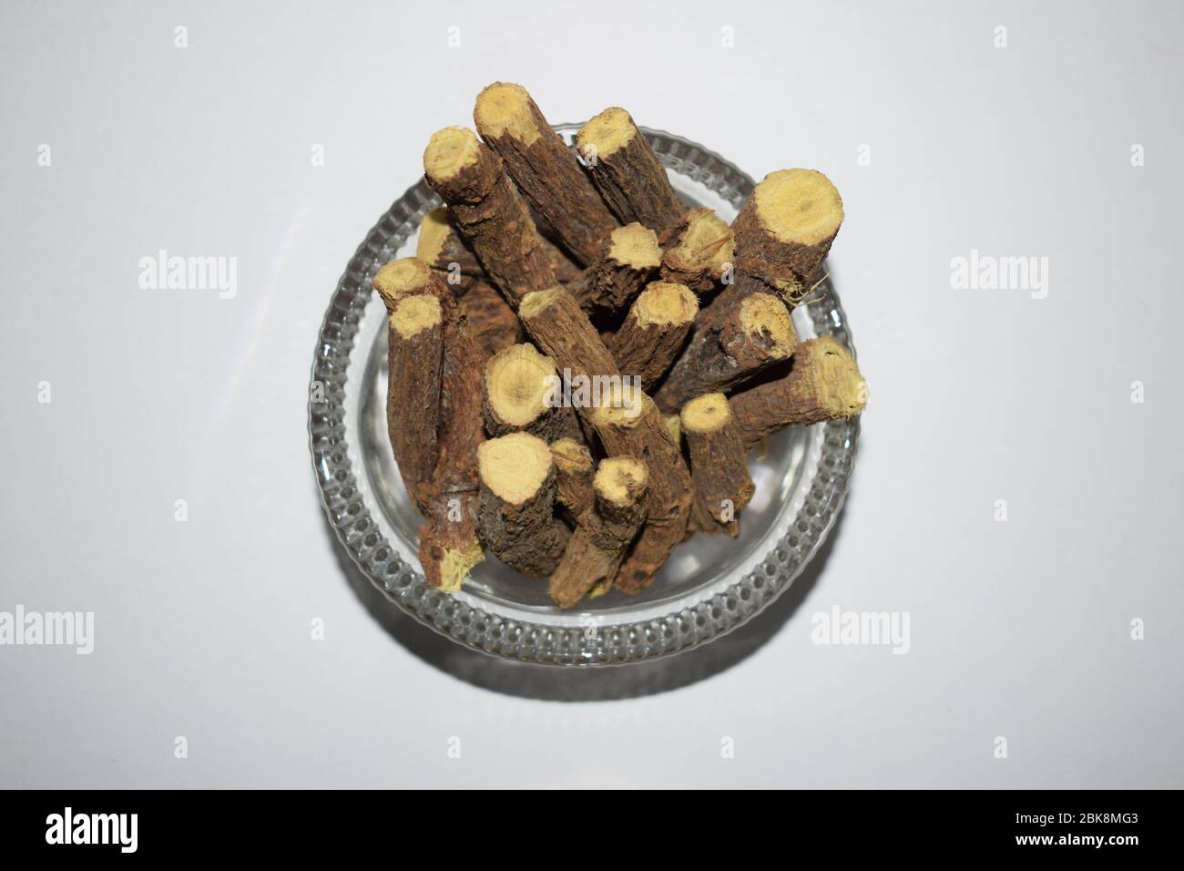 Bastone di radice di liquirizia alle erbe ayurvediche. Radici di liquirizia, glabra di Mulethi o Glycyrrhiza in una ciotola trasparente isolata su sfondo bianco.benefico per ulc Foto Stock