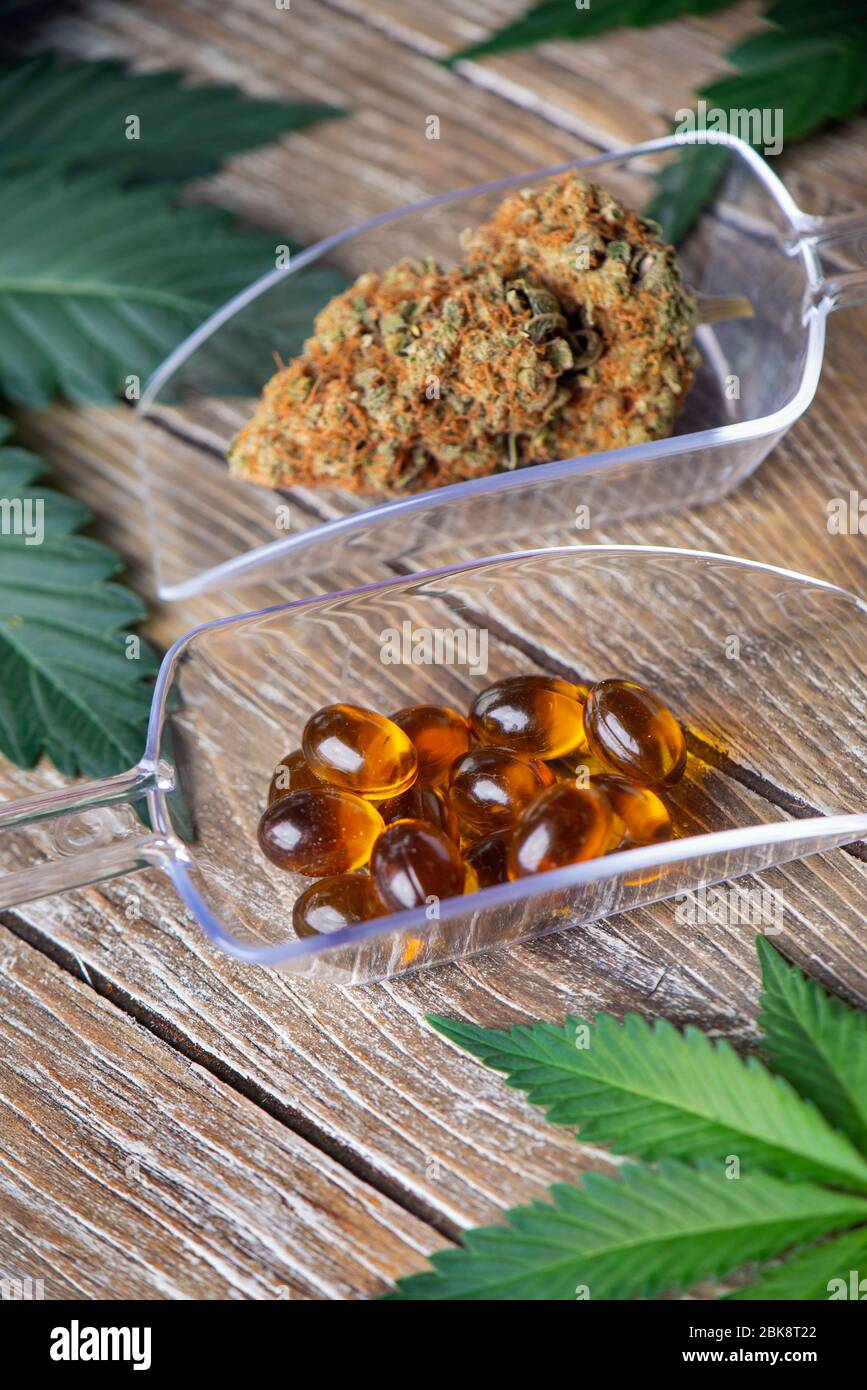 Fiori secchi di cannabis e pillole di marijuana medica con foglie verdi su sfondo di legno Foto Stock