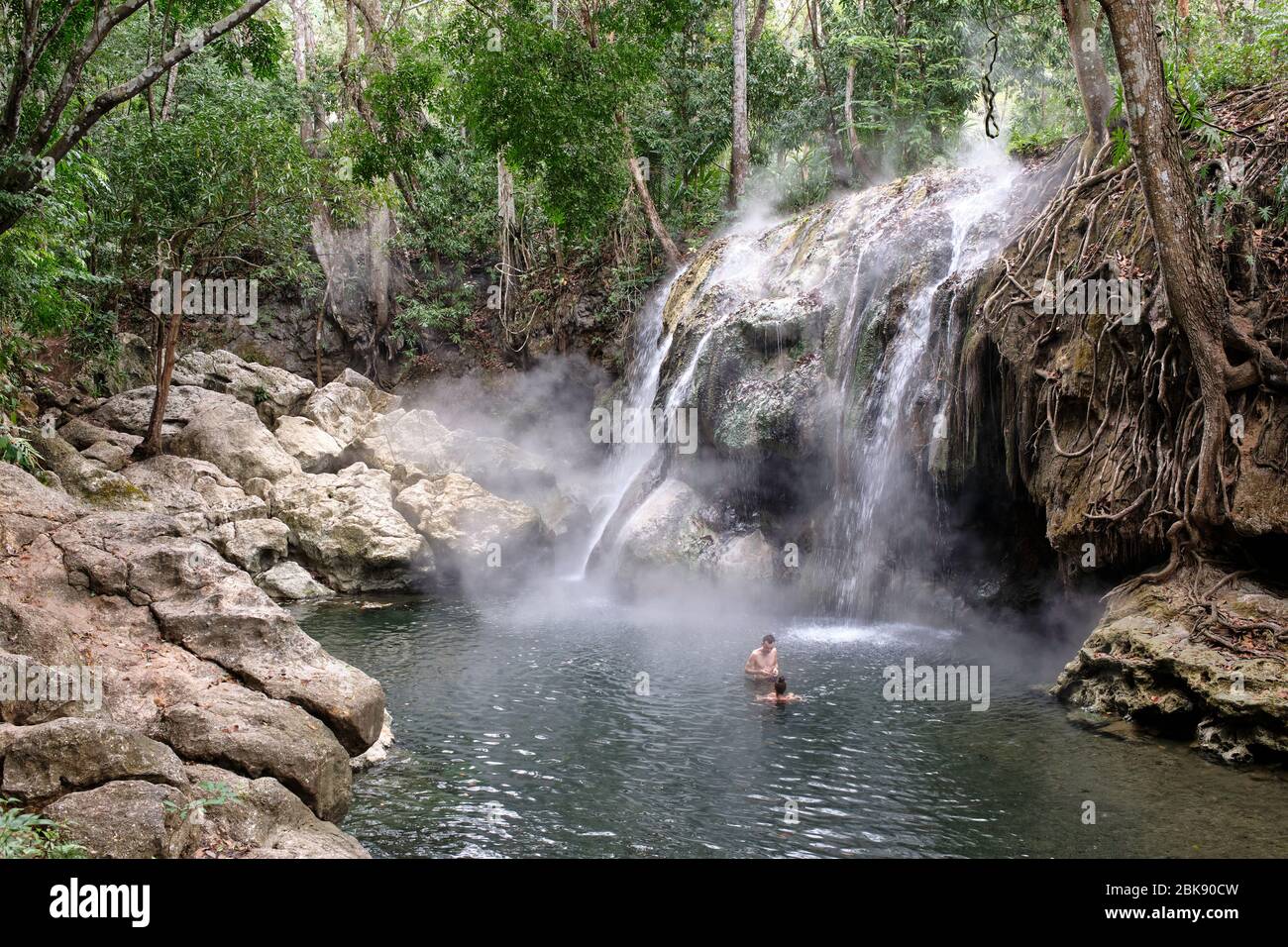 Persone che prendono un bagno in un lago dove una cascata di sorgenti calde fumanti cade. Foto Stock