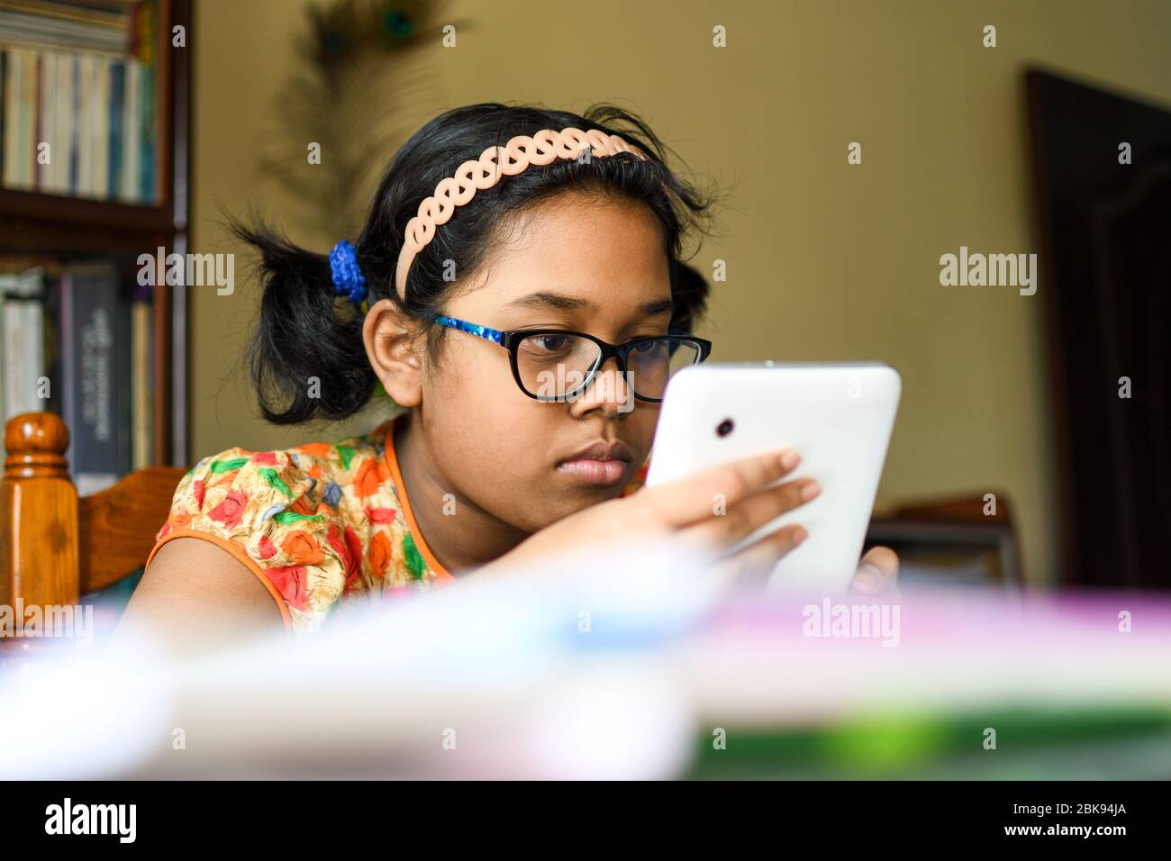 Ragazza indiana carina che studia a casa con un tablet mobile in mano Foto Stock