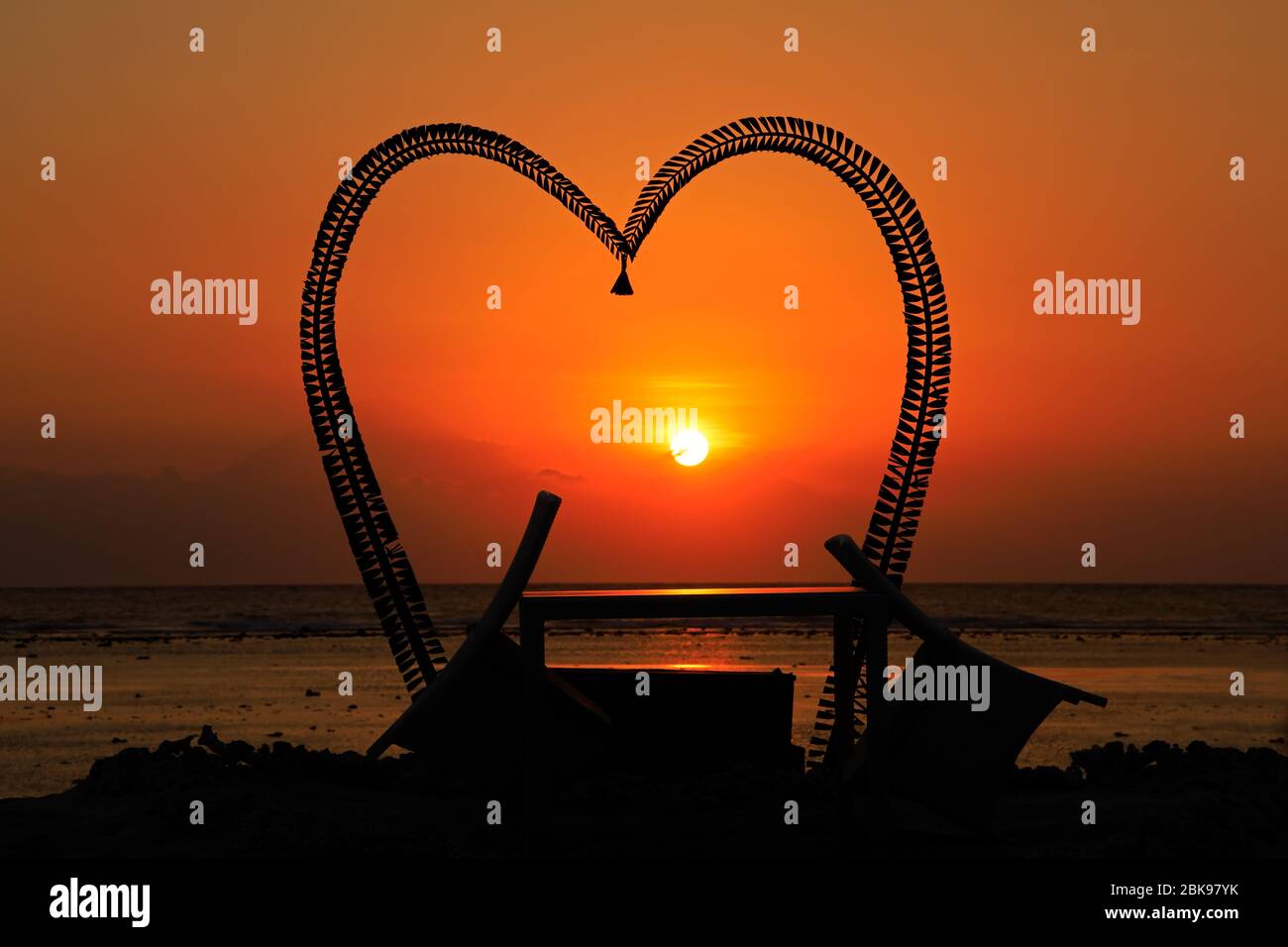 Romantica silhouette a forma di cuore con sedie su una spiaggia tropicale panoramica al tramonto Foto Stock