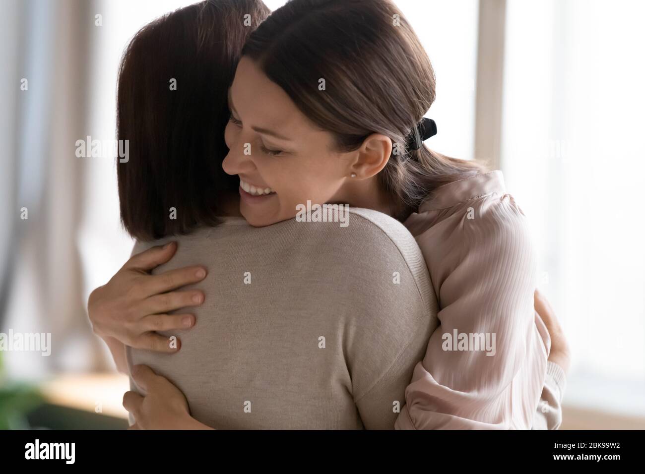 Giovane donna sorridente con occhi chiusi abbracciando madre matura Foto Stock