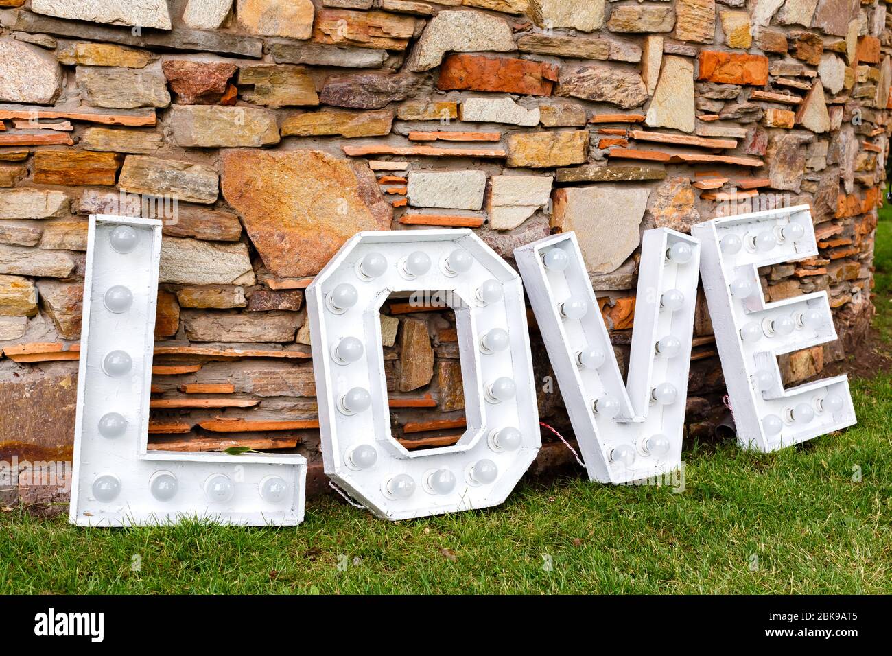 Una parola d'amore vicino al muro di pietra. Area foto in decorazione per matrimoni nel parco Foto Stock