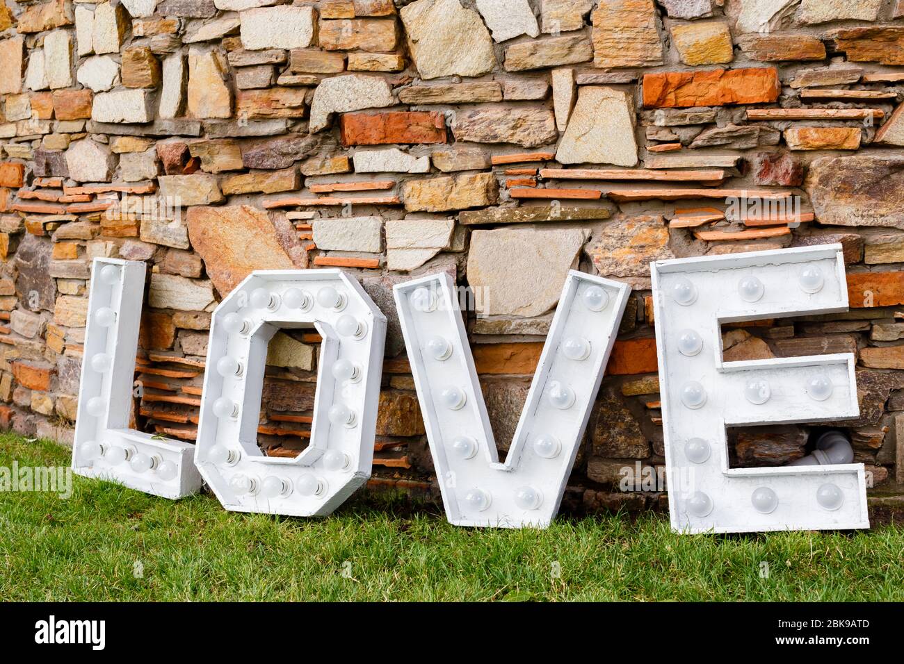 Una parola d'amore vicino al muro di pietra. Area foto in decorazione per matrimoni nel parco Foto Stock