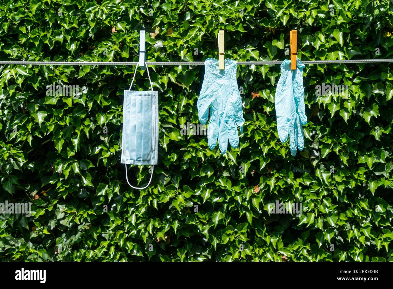 una maschera e un paio di guanti appesi su un filo in giardino Foto Stock