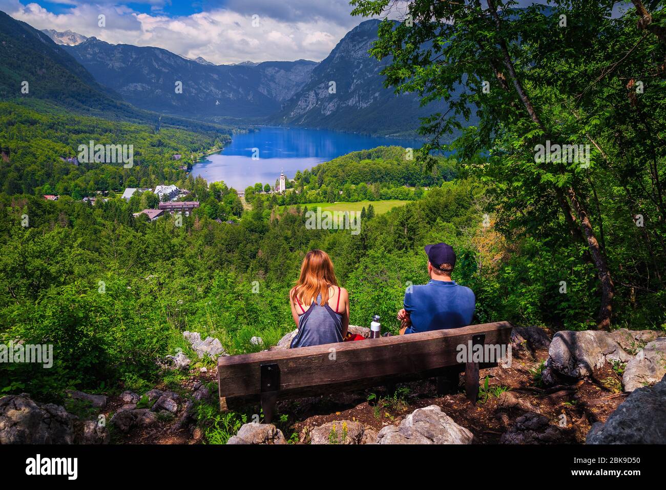 Meraviglioso luogo di escursioni con allegra coppia escursionista sulla panchina godendo la vista dalla collina, lago di Bohinj, Slovenia, Europa Foto Stock
