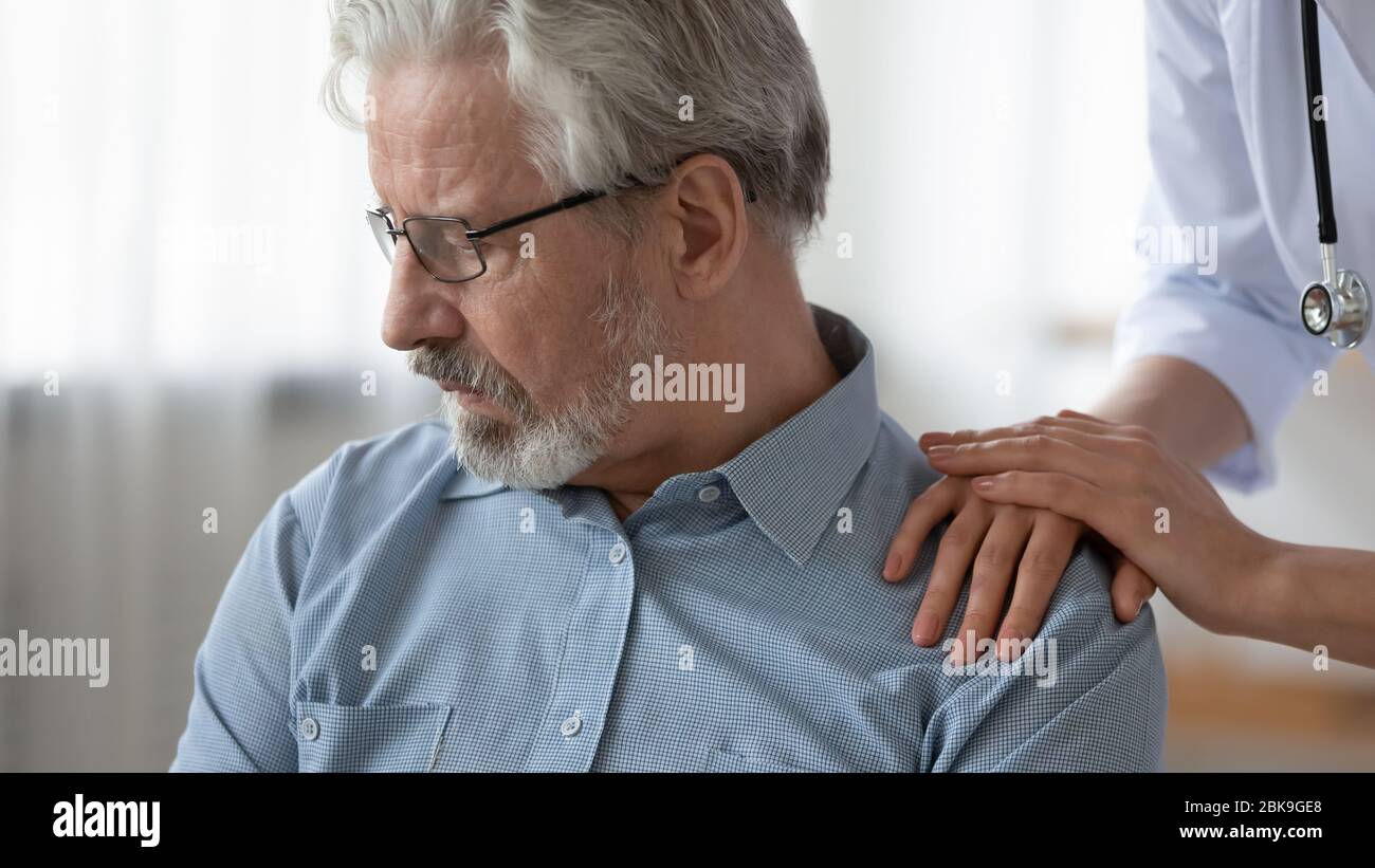 Medico femminile mani a contatto con la spalla di pazienti anziani depressi, primo piano Foto Stock