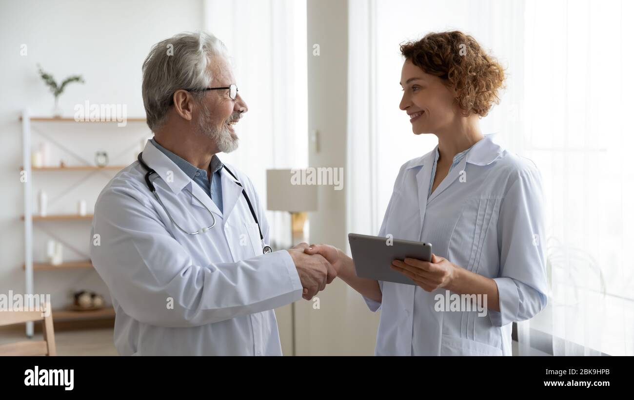 Medico senior felice medico di sesso maschile handshaking giovane infermiera femminile Foto Stock