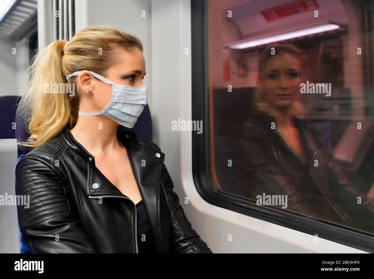 FOTOMONTAGGIO, Donna con maschera facciale, seduta in treno, riflessa nella finestra della S-Bahn SENZA maschera facciale, Corona Crisis, Stoccarda Foto Stock