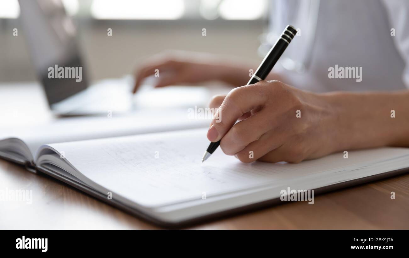 Medico femminile prendere appunti a mano nel giornale utilizzando il laptop Foto Stock